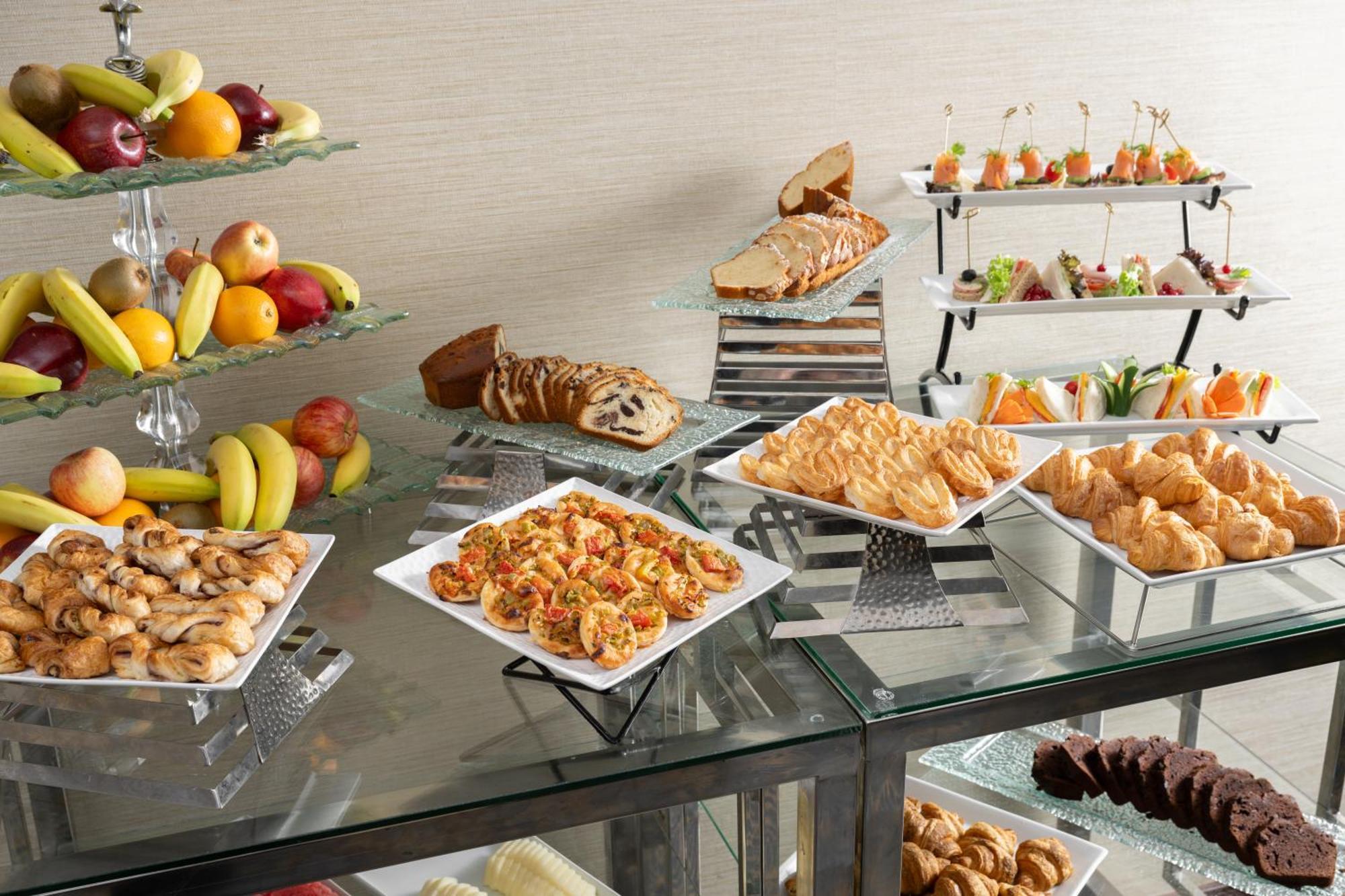 Al Aqeeq Madinah Hotel Medína Exteriér fotografie The photo showcases a buffet-style spread featuring a variety of food items. There are several platters with appetizers, including seafood dishes, pastries, and other savory items. In addition, there is a selection of fresh fruit displayed on a glass