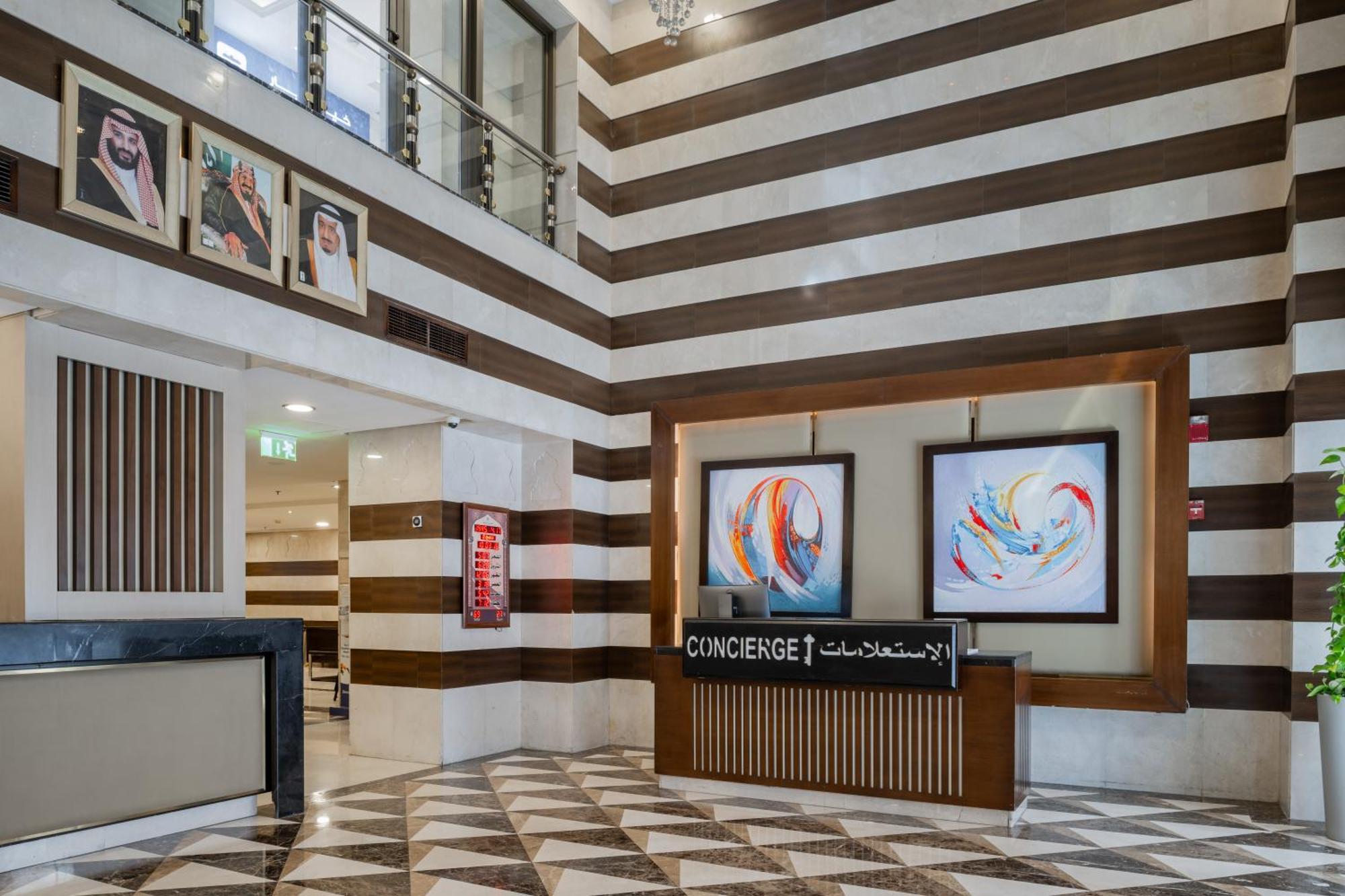 Al Aqeeq Madinah Hotel Medína Exteriér fotografie The photo shows a modern hotel lobby area characterized by its stylish design. The walls feature a pattern of horizontal stripes in different shades, creating a sophisticated atmosphere. To the left, there is a reception area with a sleek desk labele
