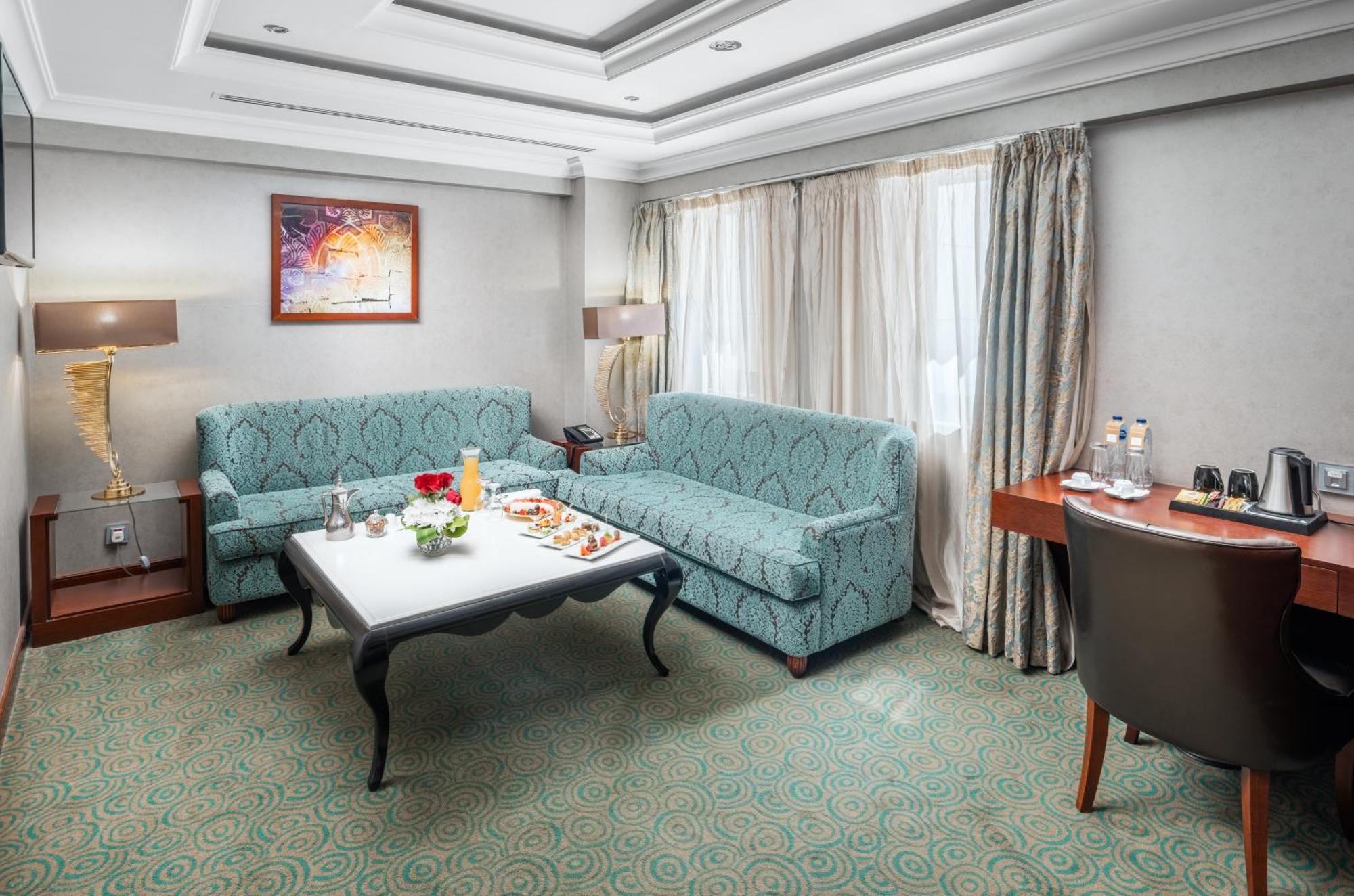 Al Aqeeq Madinah Hotel Medína Exteriér fotografie The photo shows a cozy hotel room or lounge area. It features two light blue sofas arranged around a low coffee table. On the table, there are snacks or refreshments arranged aesthetically. The room has a neutral color palette with a textured carpet 