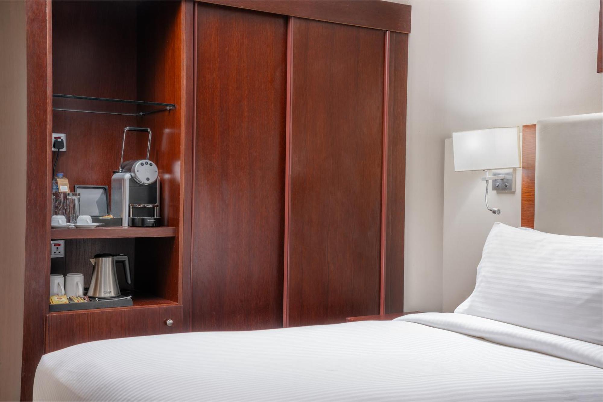 Al Aqeeq Madinah Hotel Medína Exteriér fotografie The photo shows a hotel room with a minimalist design. On the left side, there's a wooden cabinet with sliding doors that houses a small coffee maker and additional amenities, such as cups and a kettle. The bed is neatly made with white bedding and i