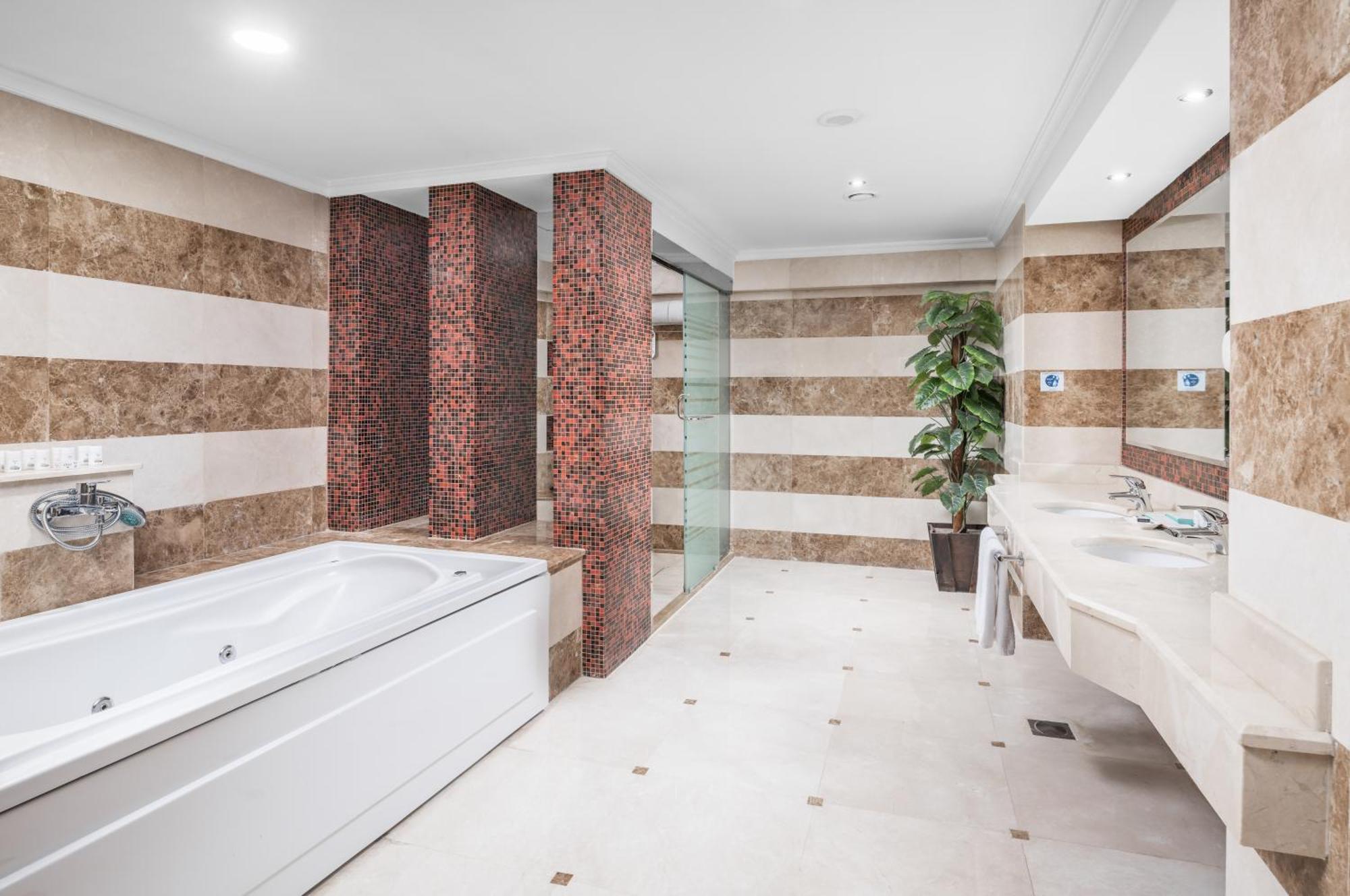 Al Aqeeq Madinah Hotel Medína Exteriér fotografie The photo shows a modern bathroom featuring a spacious layout. On one side, there is a large, white bathtub adjacent to a textured wall with warm, earthy tones. The walls are decorated with alternating horizontal stripes of light and dark colors. 

I