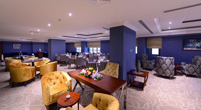 Al Aqeeq Madinah Hotel Medína Exteriér fotografie The photo shows a stylish interior of a restaurant or dining area. It features elegantly arranged seating with plush, gold-colored chairs and a wooden table at the center, adorned with a floral arrangement. The background includes more dining tables,