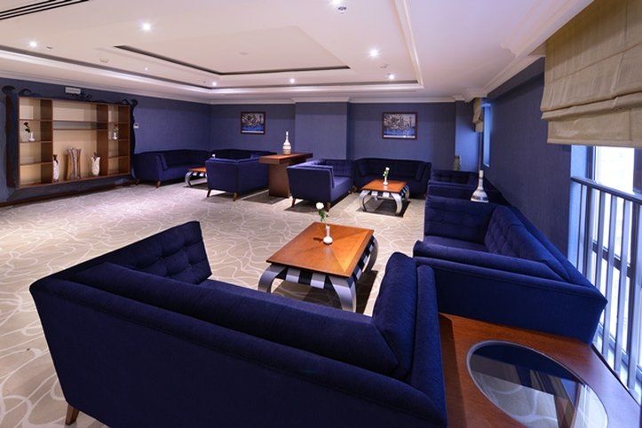 Al Aqeeq Madinah Hotel Medína Exteriér fotografie The photo shows a modern lounge area featuring a sophisticated design. The room is painted in a deep blue color, creating a calm and elegant atmosphere. There are several dark blue sofas arranged around a central wooden coffee table. The table is dec