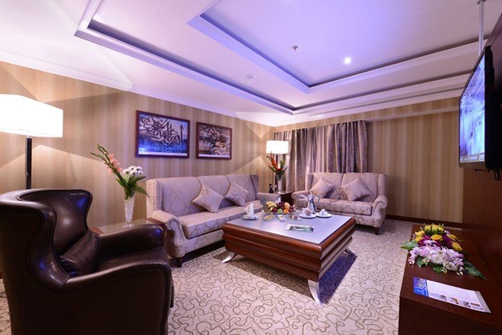Al Aqeeq Madinah Hotel Medína Exteriér fotografie The photo shows a stylish and comfortable living room. It features two light-colored sofas with decorative cushions arranged around a modern coffee table. In one corner, there's a dark, leather armchair. The walls are adorned with framed artwork, and