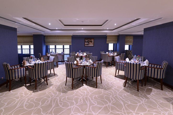 Al Aqeeq Madinah Hotel Medína Exteriér fotografie The photo shows an elegant dining room equipped with several tables. Each table is set with white tableware and neatly arranged silverware, giving a formal dining appearance. The decor features striped chairs and a carpet with a subtle pattern. The w