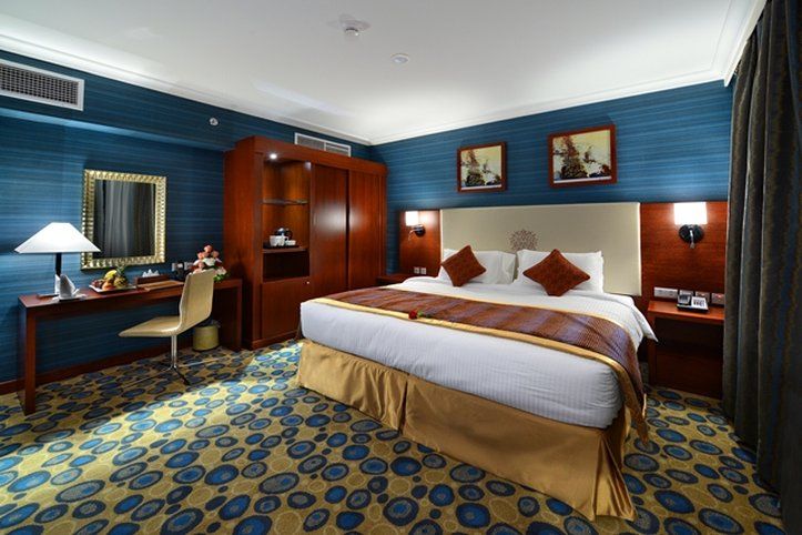 Al Aqeeq Madinah Hotel Medína Exteriér fotografie The photo shows a hotel room designed with a modern and stylish aesthetic. It features a large bed with a cream-colored headboard and decorative pillows. The room is decorated with blue walls and patterned carpet, creating a cozy atmosphere. 

There 