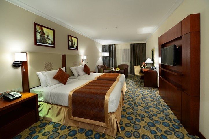 Al Aqeeq Madinah Hotel Medína Exteriér fotografie The photo shows a hotel room featuring two beds with white linens and brown throw blankets. There are decorative pillows on the beds. The room has a modern design, with wooden furniture including bedside tables and a large wooden unit that houses a t